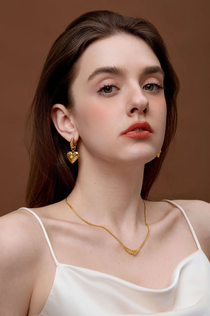 Woman wearing SUIHE Jewelry Amour Pendant Earrings with heart charm and starburst design in gold-tone finish.