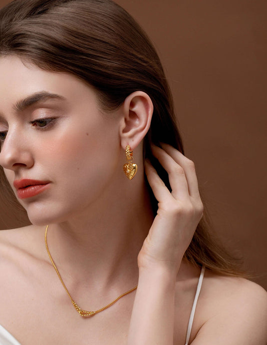 Woman wearing SUIHE Jewelry's Amour Pendant Earrings with heart charm and crystal, in a gold-tone finish, adding elegance to her look.