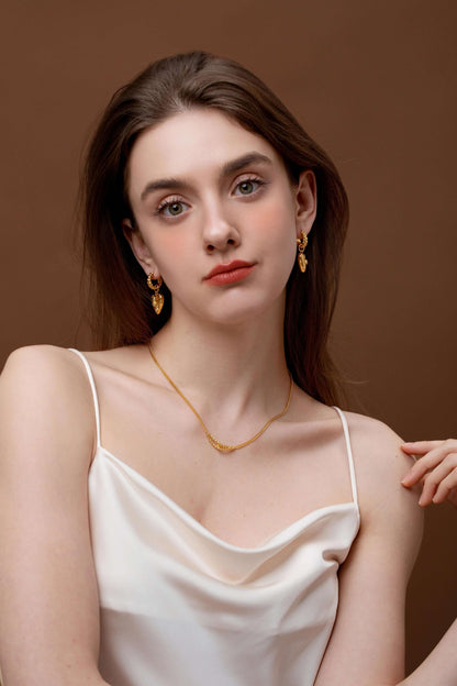Woman wearing "Amour" Pendant Earrings by SUIHE Jewelry with heart charm and starburst design in a gold-tone finish.