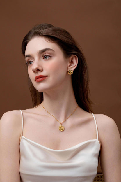 Elegant woman wearing a gold medallion necklace and matching earrings, styled with a soft white top, showcasing timeless fashion.