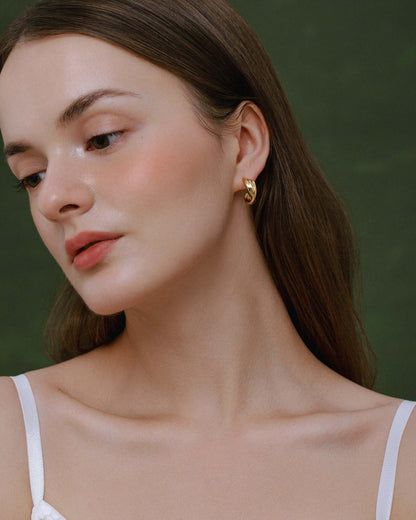 Model wearing SUIHE Jewelry's Wavelet Hoop Earrings, featuring a gold wave-inspired design, reflecting light for a sophisticated look.