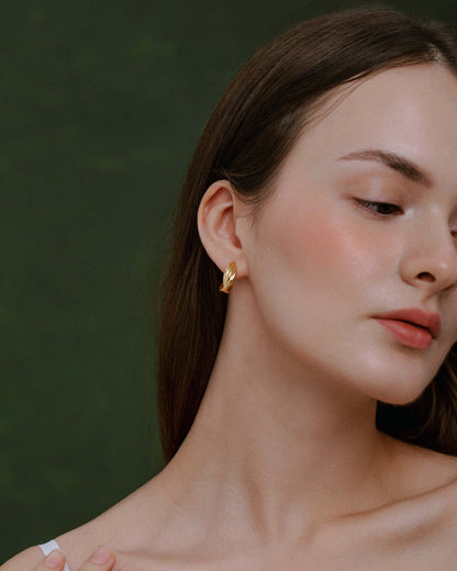 Woman wearing Wavelet Hoop Earrings by SUIHE Jewelry, featuring a wave-inspired design in high-polish gold against a green background.
