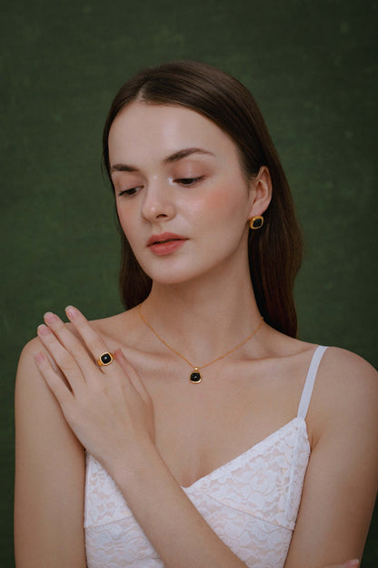 Woman wearing SUIHE Jewelry Black Onyx Square Ring and matching necklace, showcasing elegance and style against a green background.