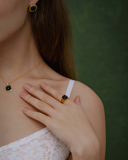 Woman wearing SUIHE Jewelry "Nocturne" Black Onyx Square Ring and matching necklace and earrings on a green background.
