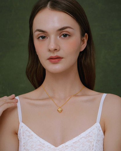 Woman wearing SUIHE Jewelry Amour Heart Pendant Necklace on gold chain, showcasing elegance and timeless style, against a dark green background.