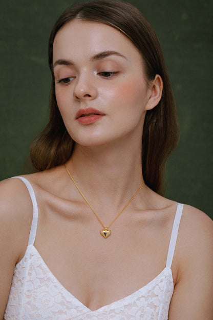 Woman wearing SUIHE Jewelry "Amour" Heart Pendant Necklace with a golden heart on a delicate gold chain, showcasing sophistication and style.