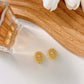 Golden Tulip clip earrings by SUIHE Jewelry in 18k gold vermeil, showcasing tulip embossed design, placed on a wooden surface with white flowers.